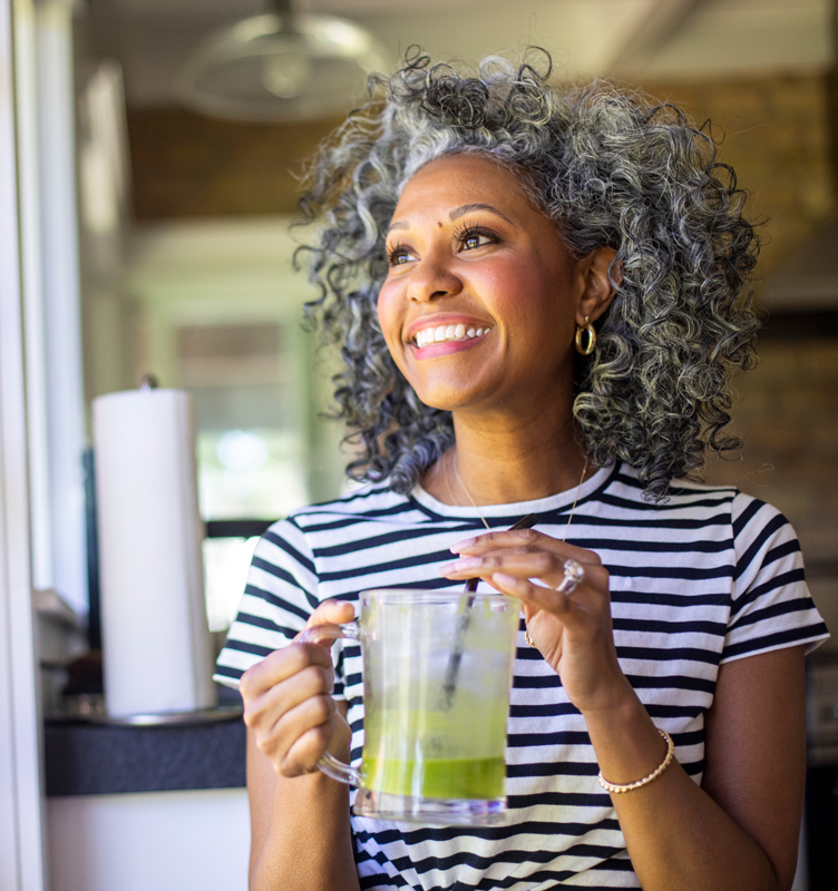 woman smiling while drinking a green smoothie in her home