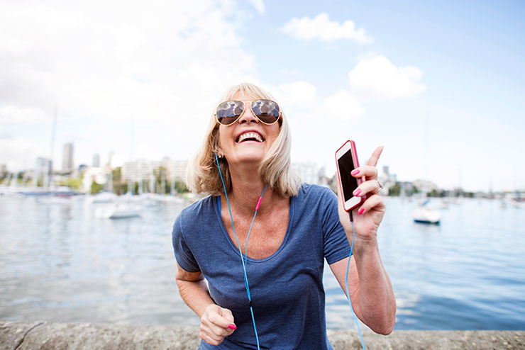 Mujer madura sonriendo y bailando con los auriculares en su teléfono