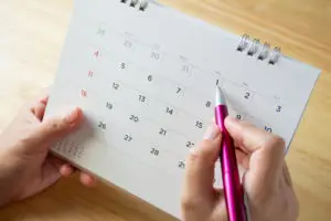 A calendar page with an individual's hand holding a pen