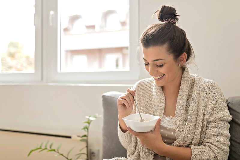 Mujer joven comiendo avena por la mañana y sonriendo en casa