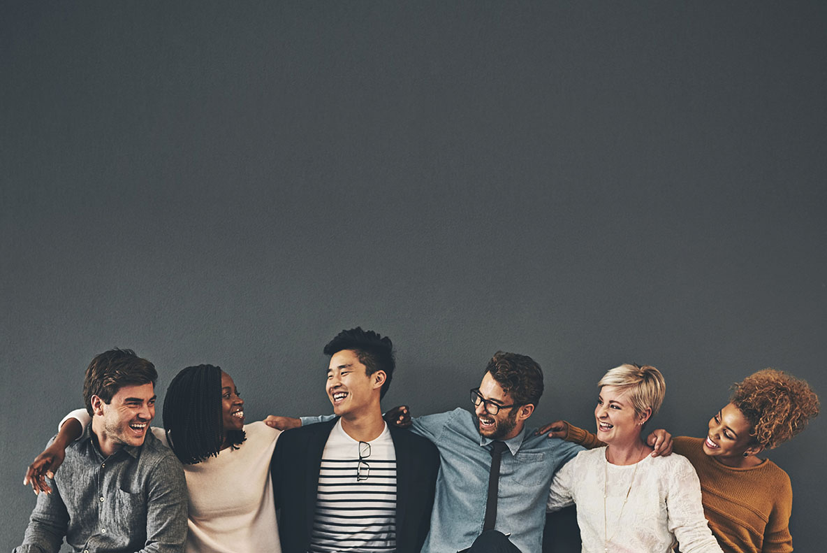 A group of diverse young people smiling at each other in a line with their arms on each other's shoulders