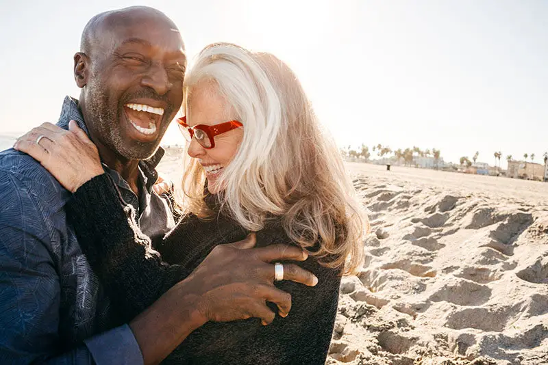 Una pareja de ancianos abrazados y riendo en la playa
