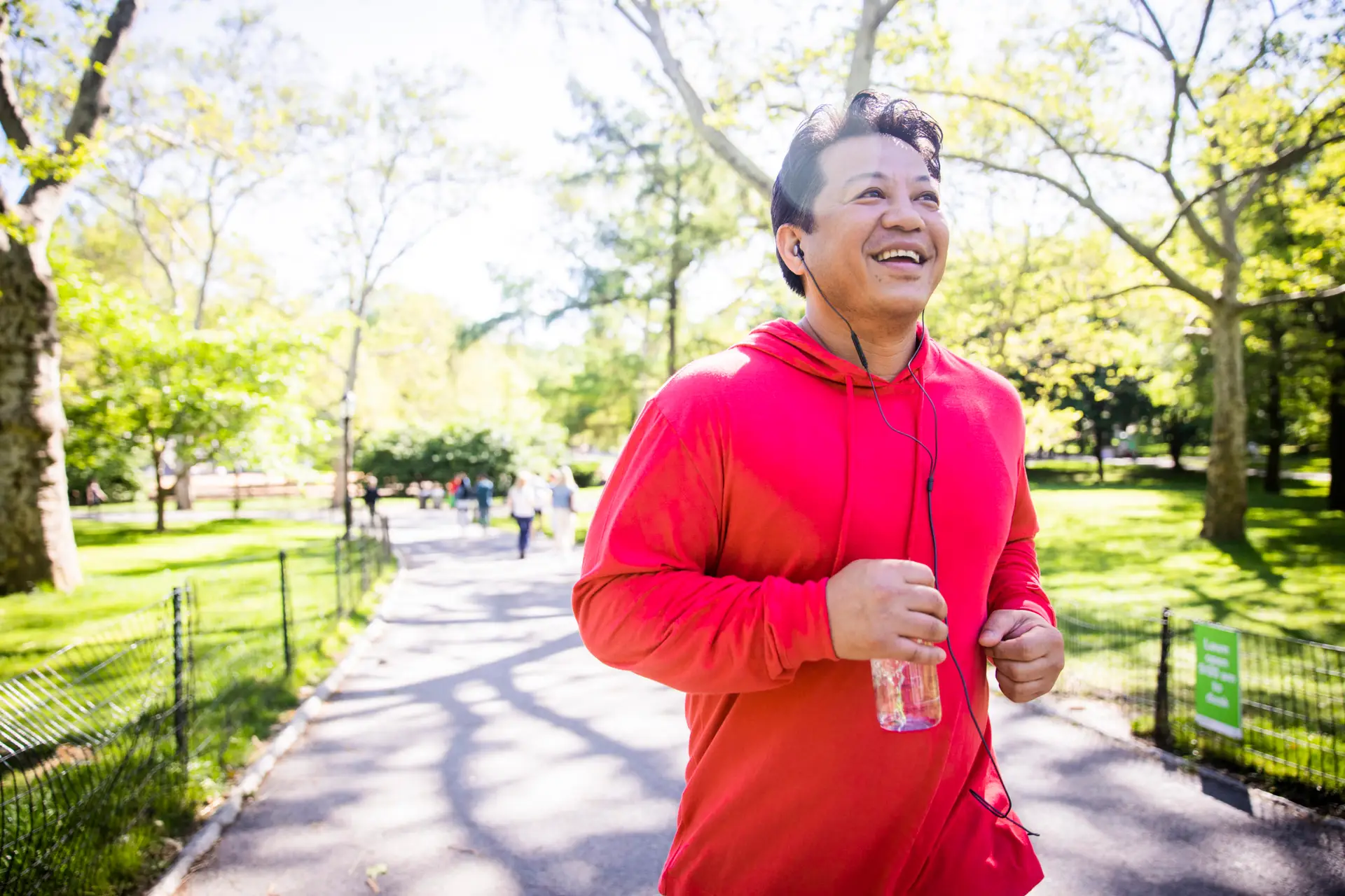 A man jogging at a park with headphones and holding a bottle of water