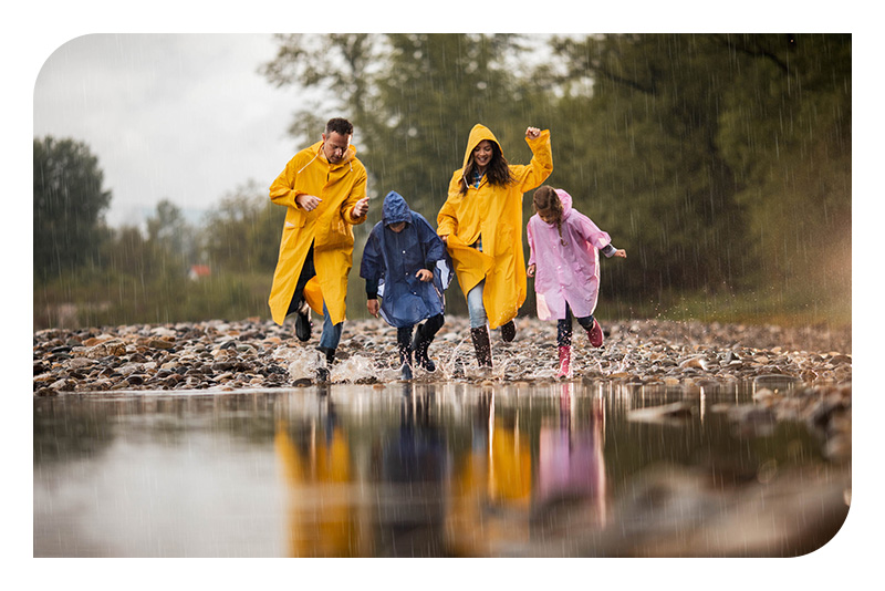 Una familia de cuatro miembros paseando bajo la lluvia con chubasqueros