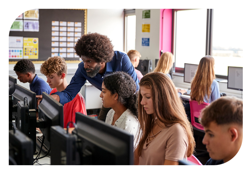 A group of students on computers with a teacher helping troubleshoot