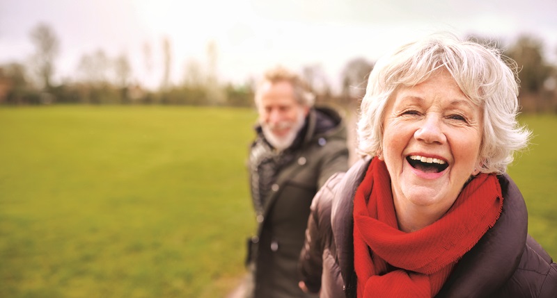 Portrait Of Loving Senior Couple Enjoying Autumn Or Winter Walk Through Park Together