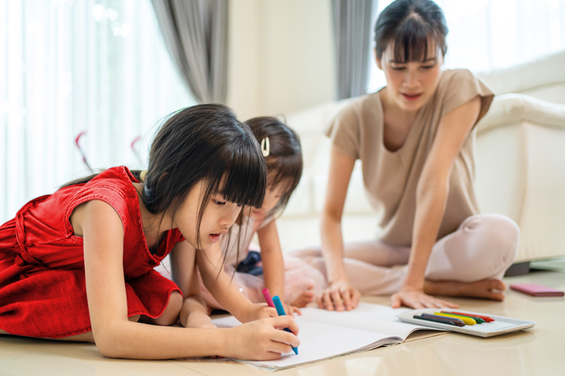 A mother and two young daughters coloring on the floor