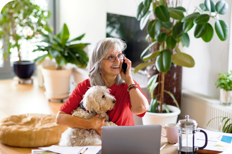 A senior woman holding a dog while on the phone at home