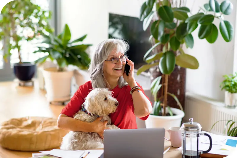 Una mujer mayor con un perro en brazos mientras habla por teléfono en casa