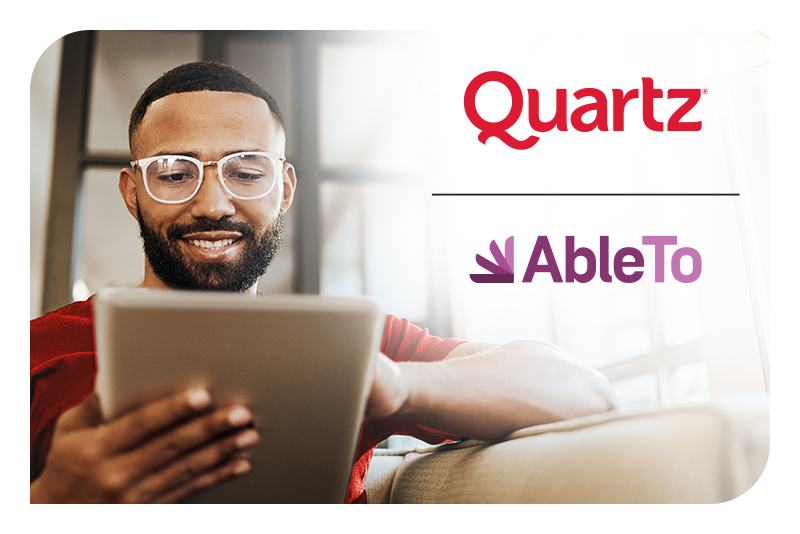 A man sitting on a couch using a tablet with Quartz - AbleTO logo
