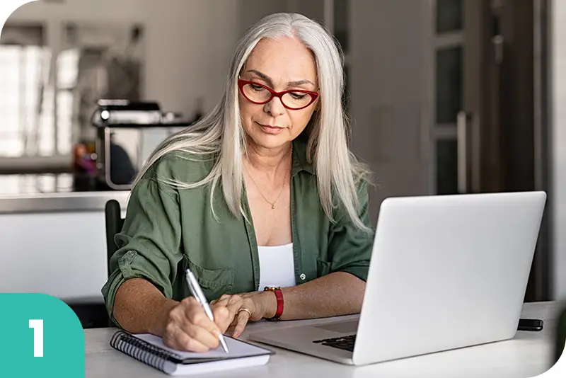 Una mujer mayor escribe en un bloc de notas en la mesa de su casa