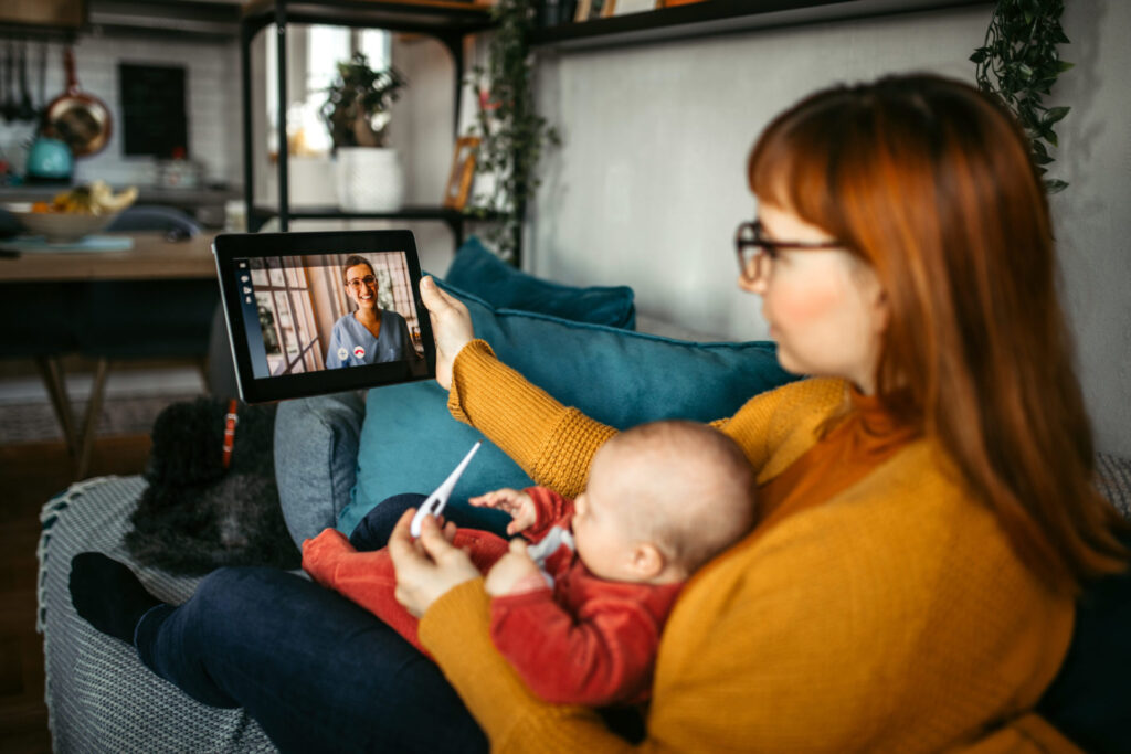 A mother and child sitting on a couch on a video call with a healthcare professional