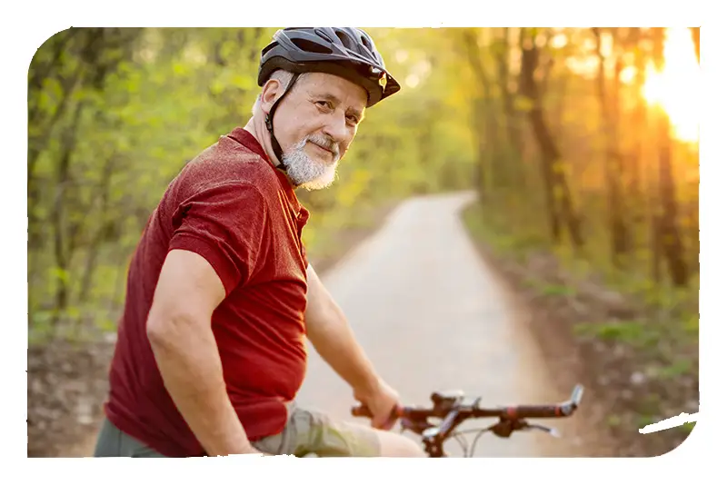 A senior person on a bicycle headed down a paved trail through the forest.