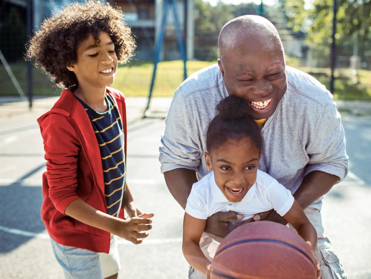 A grandfather playing basketball with his grandchildren at the park