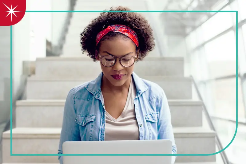 A woman sitting on steps using a laptop with a Quartz spark icon with a teal outline