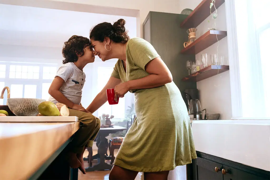 Una madre y un hijo pequeño con las cabezas tocándose sonriéndose en una cocina