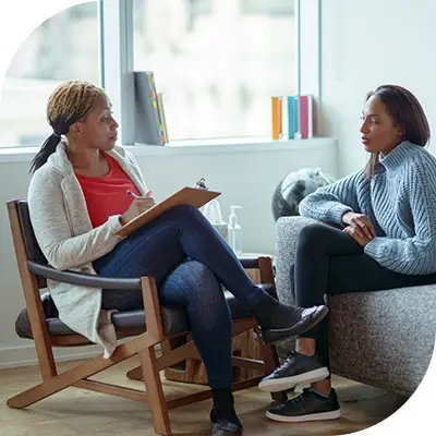 Counselor with a clipboard listening to a person on a gray sofa who is a patient.