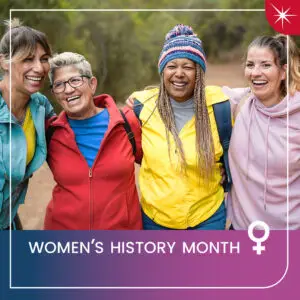 Four women in hiking gear hold each other up by the shoulders and laugh.