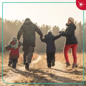 Family in cold weather gear hiking down a forest trail. A teal board with the Quartz spark is around the photo.