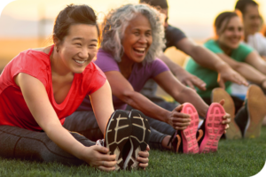 Two persons stretch during an outdoor fitness activity. They are wearing sportswear and smiling