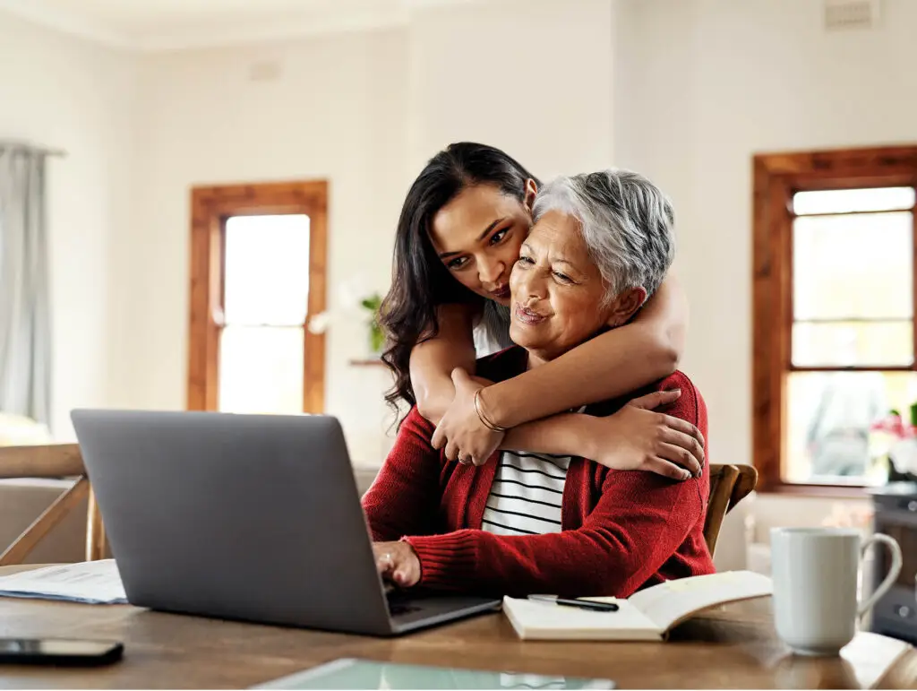 Daughter hugging mother while she is working on a laptop