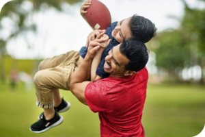 A person lifts a child up while smiling. It looks like they are playing a game of football.