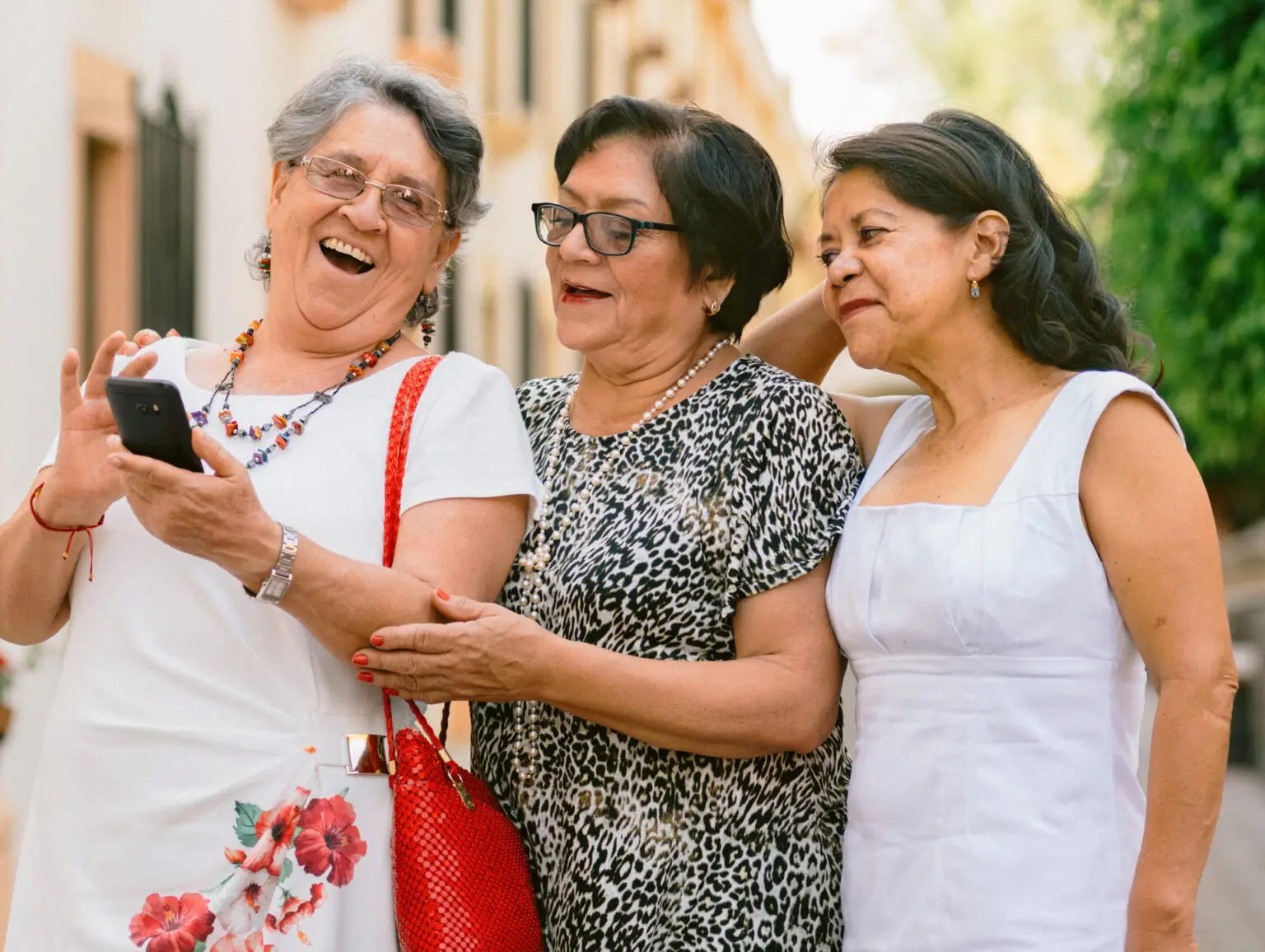 Three women looking at a phone while outside on the sidewalk