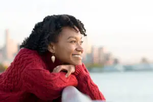 A person in a red smiles and looks relaxed as they look out at a scenic water view