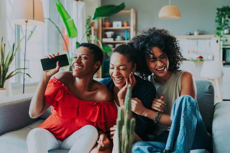 Three women laugh as they sit next to each other in a room