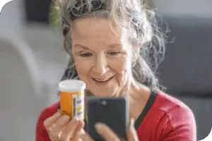A person holds a pill bottle next to their phone with a smile on their face