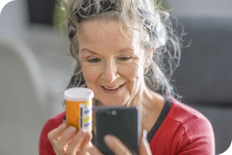 A person holds a pill bottle next to their phone with a smile on their face