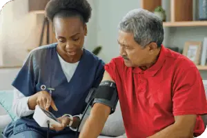 A health provider sits next to a patient as they take his blood pressure and both look at the blood pressure monitor screen
