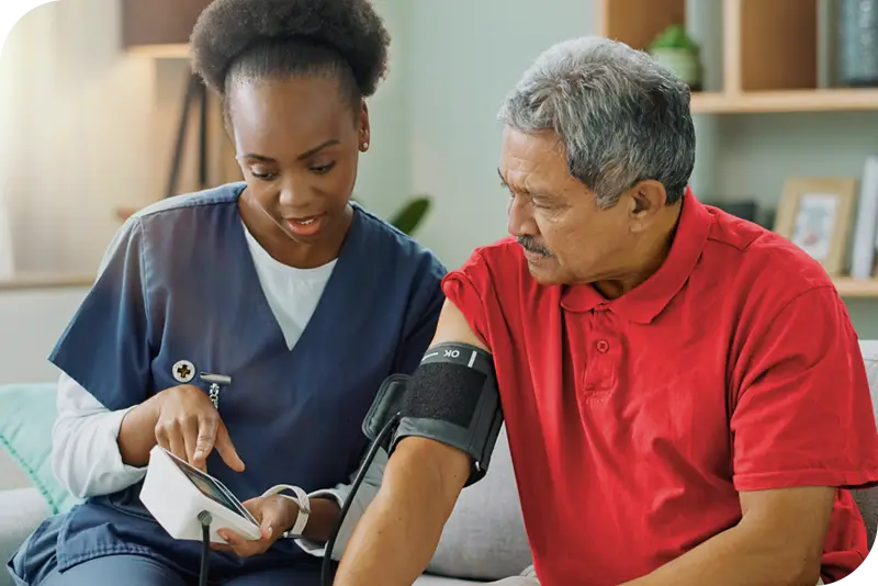 A health provider sits next to a patient as they take his blood pressure and both look at the blood pressure monitor screen