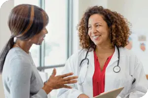 A health provider and a patient smile as they talk to one another in front of a bright window