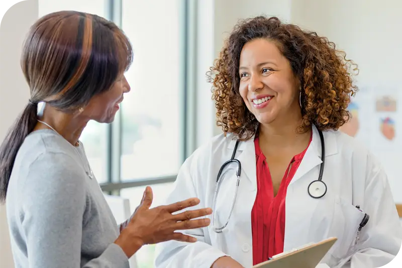 A health provider and a patient smile as they talk to one another in front of a bright window