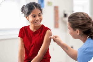 A child smiles at their health provider as they apply a bandaid to their left arm
