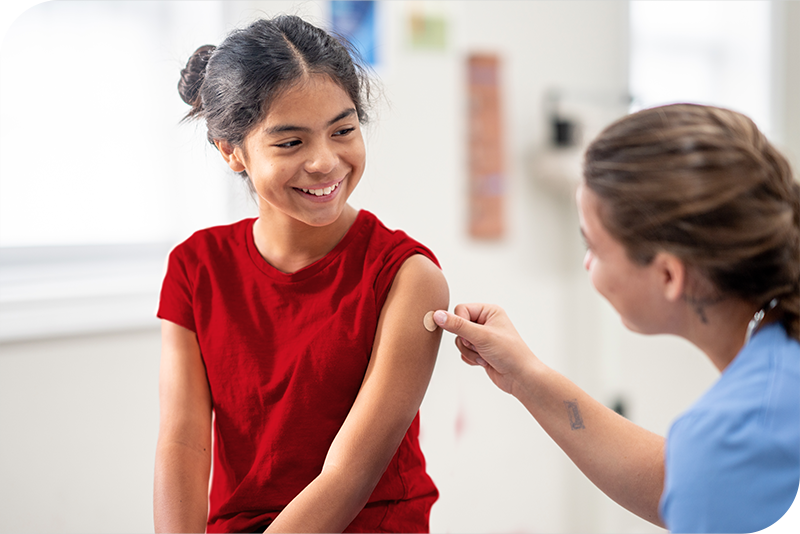 A child smiles at their health provider as they apply a bandaid to their left arm