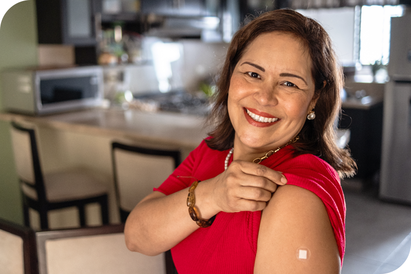 A woman smiles at the camera as she rolls up her sleeve to show a small adhesive bandage on her arm