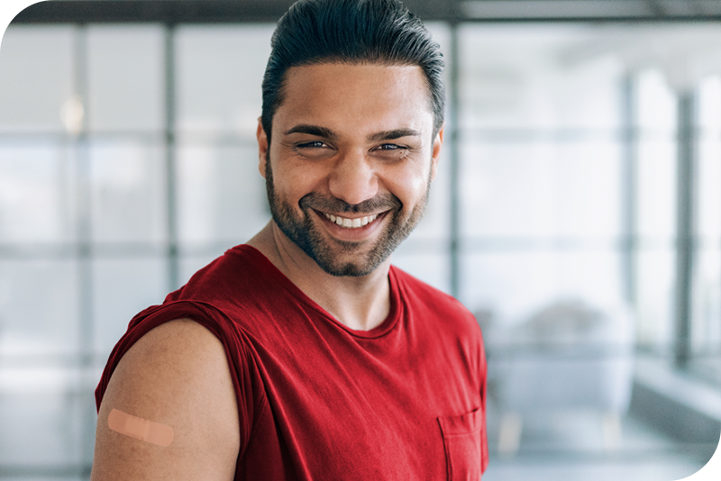A person smiles at the camera with their sleeve rolled up showing an adhesive bandage