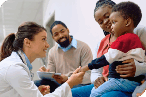 A child is surrounded by his parents as a health provider crouches in front of them and smiles