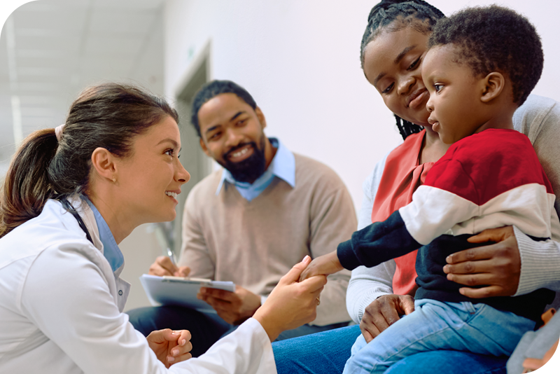 A child is surrounded by his parents as a health provider crouches in front of them and smiles