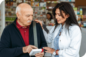 A person in a white blouse smiles as they read the back of a medication box with another