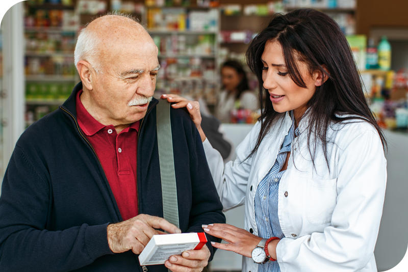 A person in a white blouse smiles as they read the back of a medication box with another