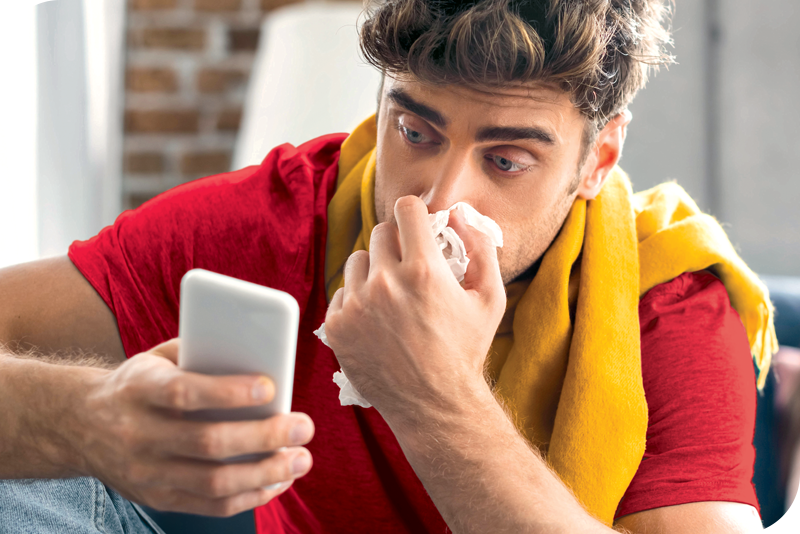 A man blows his nose as he looks at his cell phone