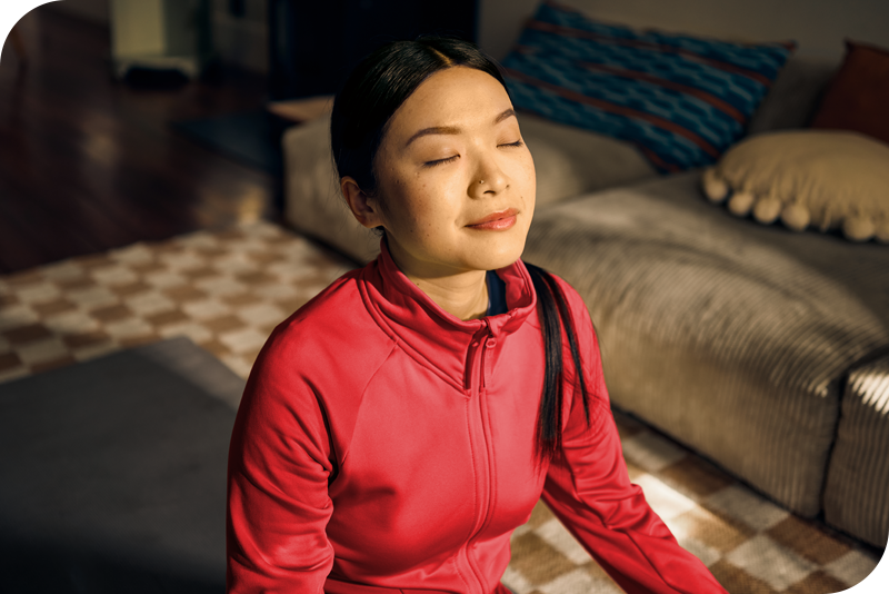 A person sits on the ground they their legs crossed, appearing to meditate as they look into a warm light