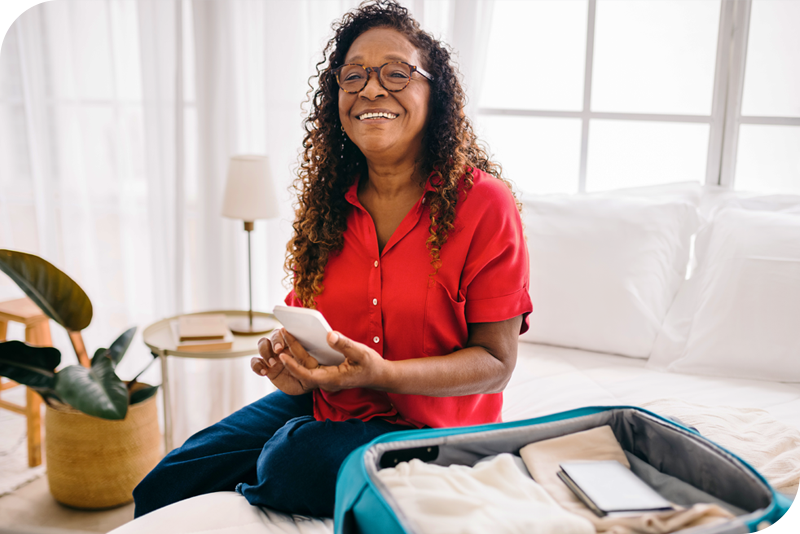 Woman sitting on a bed while packing a suitcase for a trip.