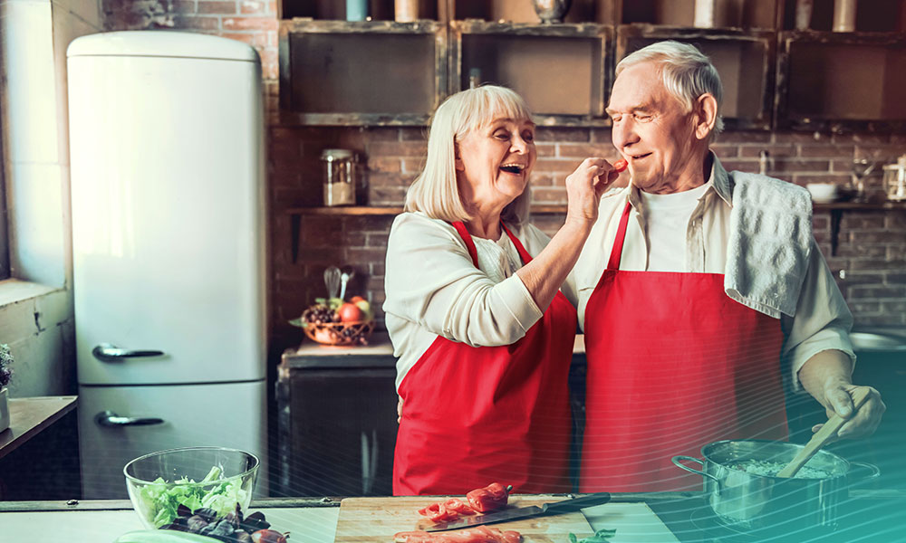 Beautiful senior couple in aprons is tasting food and smiling while cooking together in kitchen