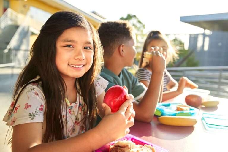 Girl at elementary school lunch table smiling to camera