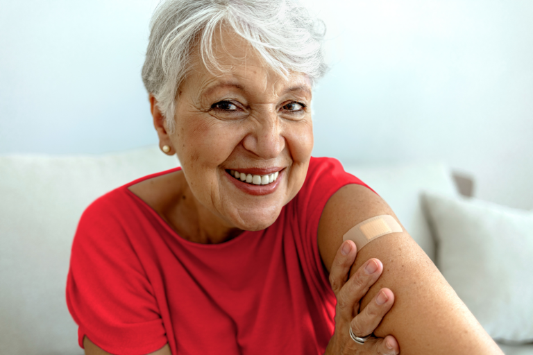 Proud mature woman smile after vaccination with bandage on arm. Beautiful smiling senior woman 70s after receiving the coronavirus vaccine. Elderly lady getting immunization via anti-viral vaccine.