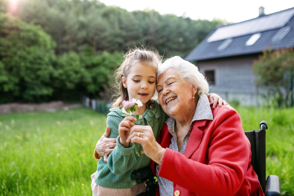 Granddaughter spending time with elderly grandma, picking widlflowers. Senior lady in wheelchair spending time in nature. Weekend in cottage.